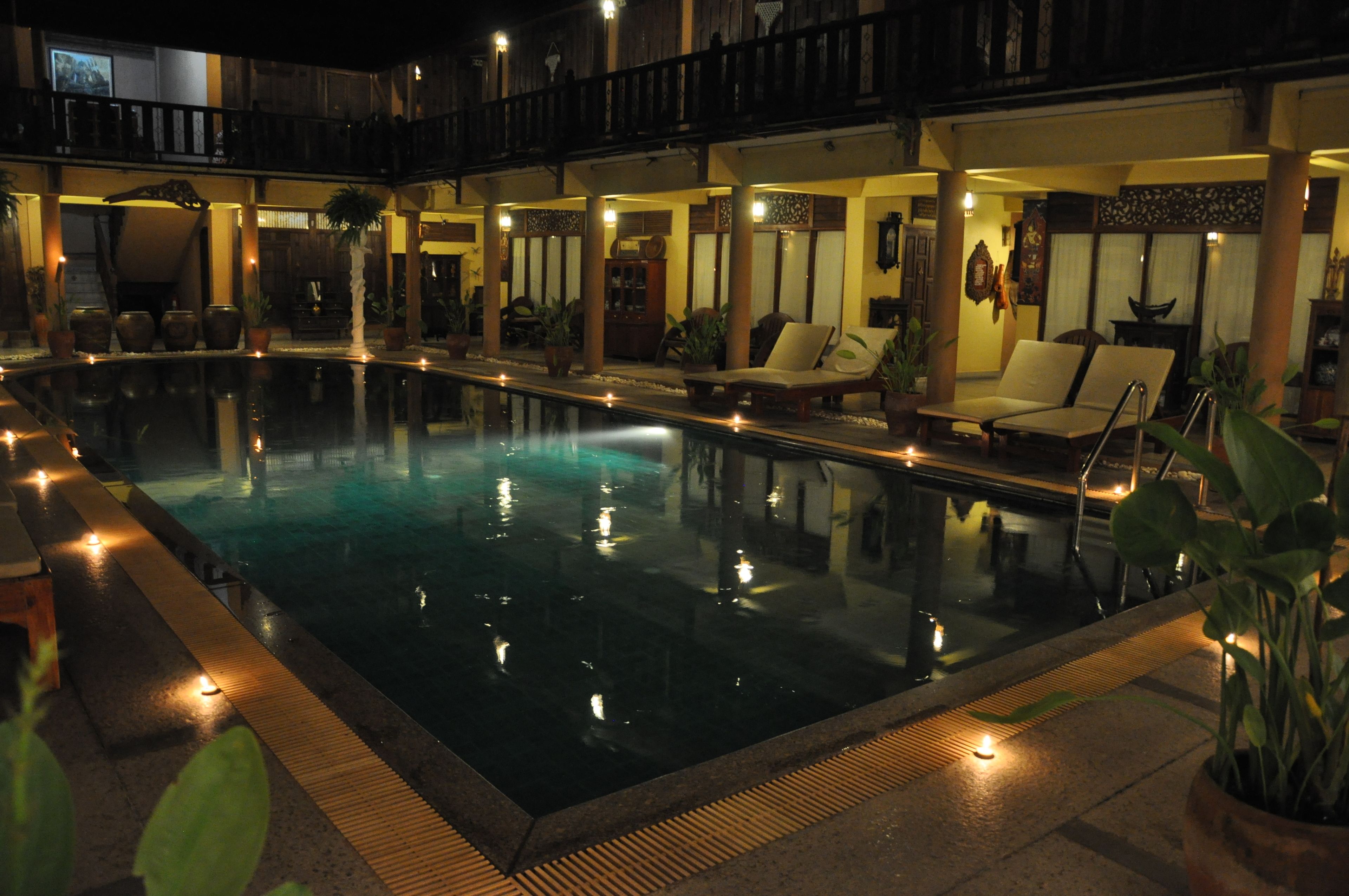 A pool area with lounge chairs and potted plants, surrounded by a wooden deck and a covered seating area.