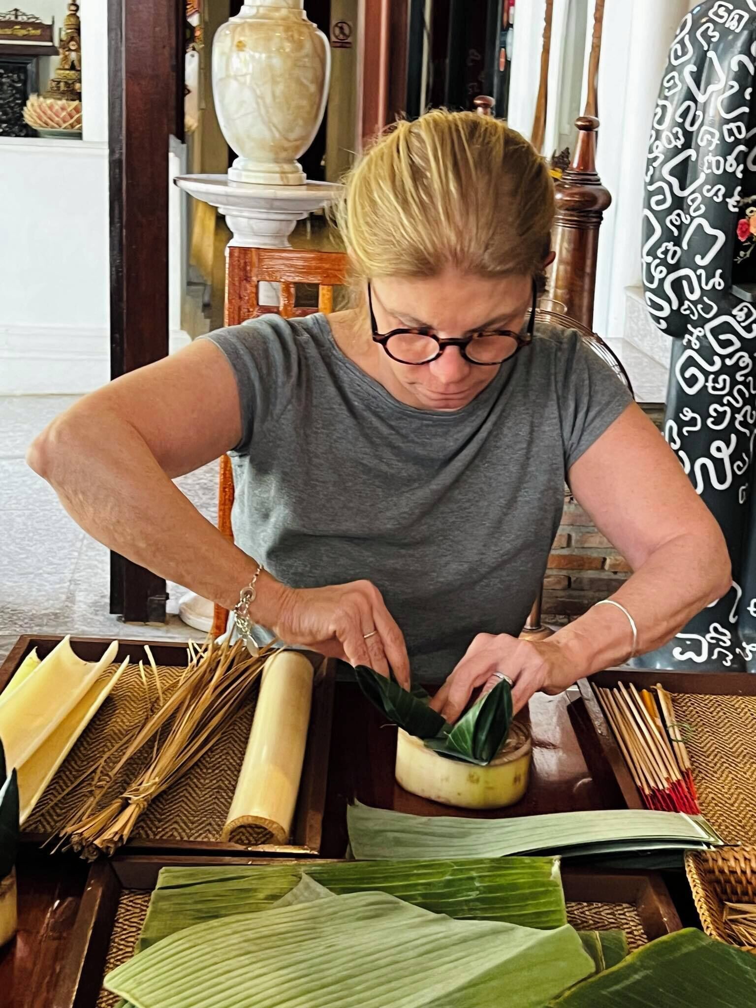 A person preparing food with a bowl and green leaves on a table.