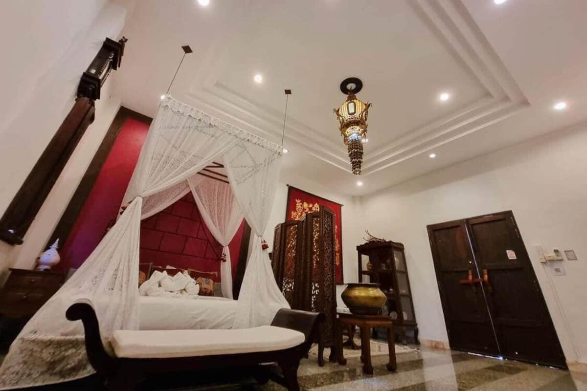 A room with a bed, a chandelier, a red accent wall, and a traditional door.