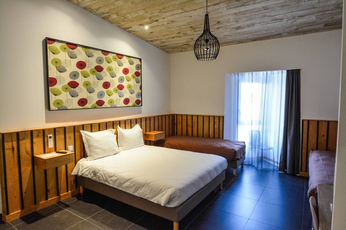 Een slaapkamer met een bed, nachtkastjes, een houten hoofdbord, een hanglamp en een groot abstract schilderij aan de muur.