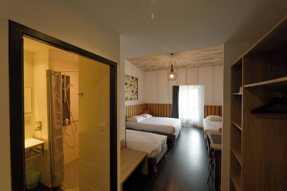Een hotelkamer met een douche, twee bedden, een houten bankje, een bureau en een kledingkast.