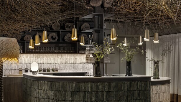 A modern bar area with a curved counter, hanging pendant lights, and decorative plants. - Le Relais Du Boisniard (Chanverrie)