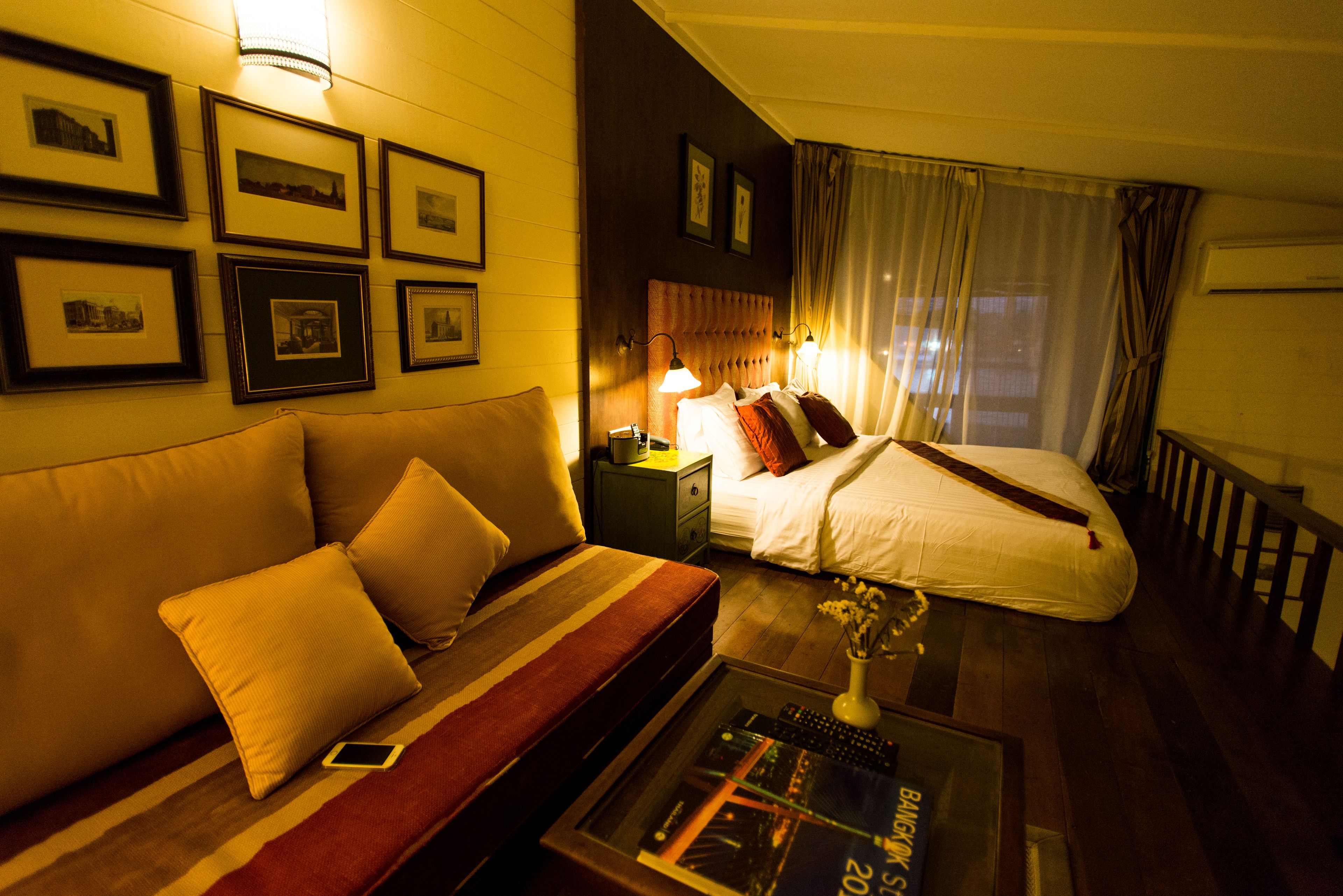 A hotel room with a sofa, a bed, a nightstand, and a coffee table with a remote control.