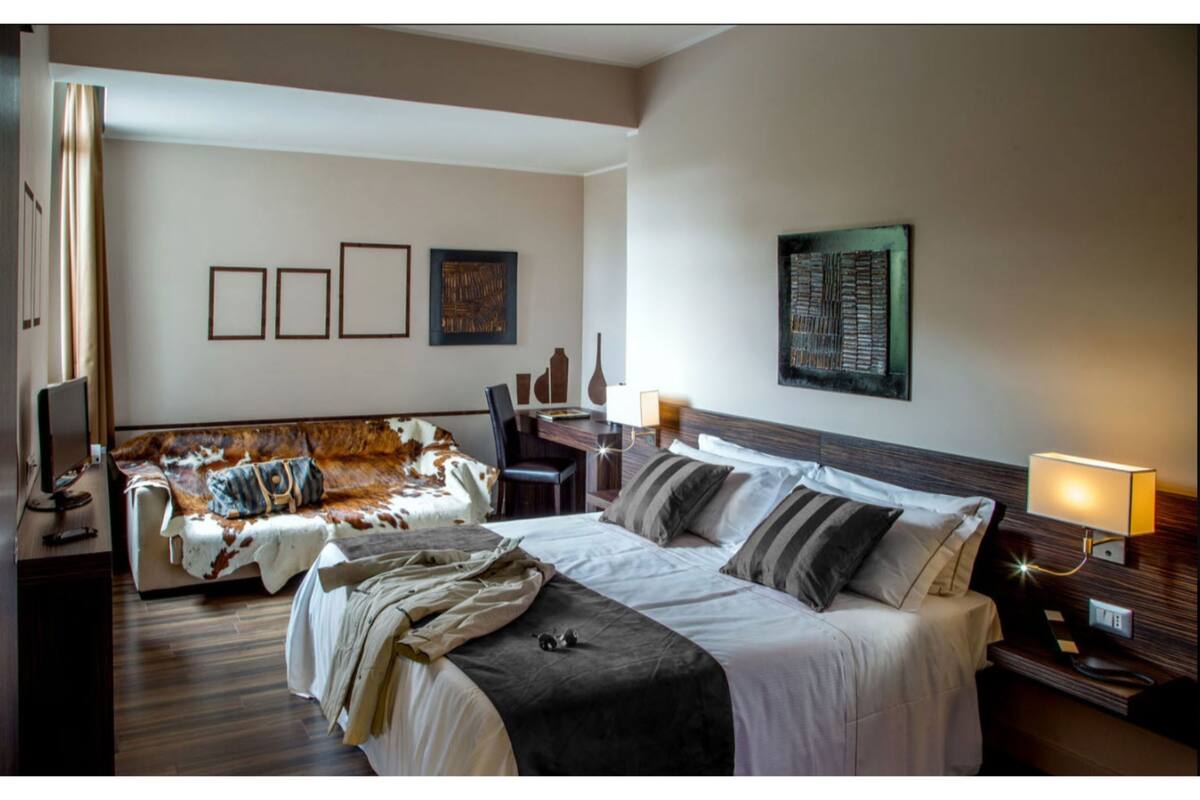 Habitació d'hotel amb un llit gran, un sofà, un escriptori i una televisió.