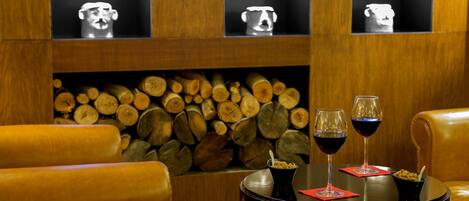 A cozy seating area with leather chairs, a round table with two wine glasses and a bowl of cereal, and a wall adorned with wooden logs and three framed items.