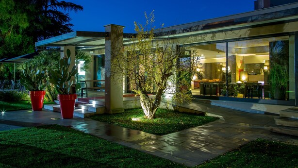 A modern building with a glass facade, outdoor seating area, and a well-maintained garden with potted plants. - Park Hotel Sabina (Magliano Sabina)