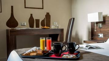 A breakfast tray with pastries, two glasses of juice, and two mugs on a bed in a hotel room.