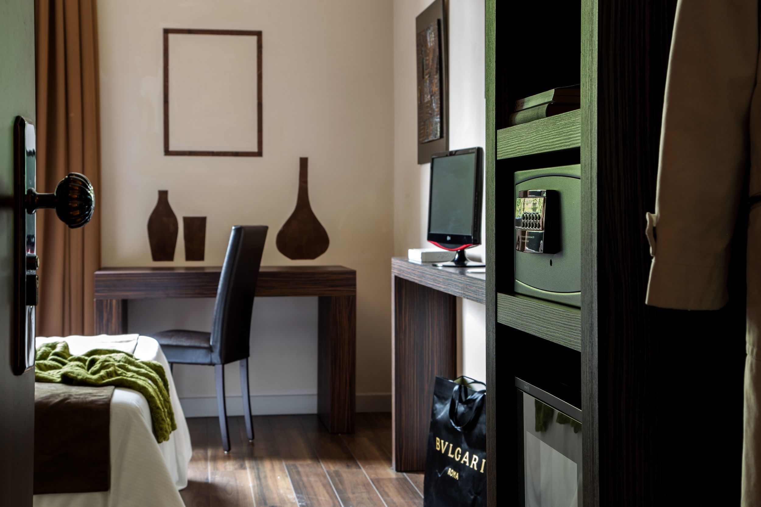 Et hotelværelse med seng, skrivebord med computer, stol og fjernsyn.