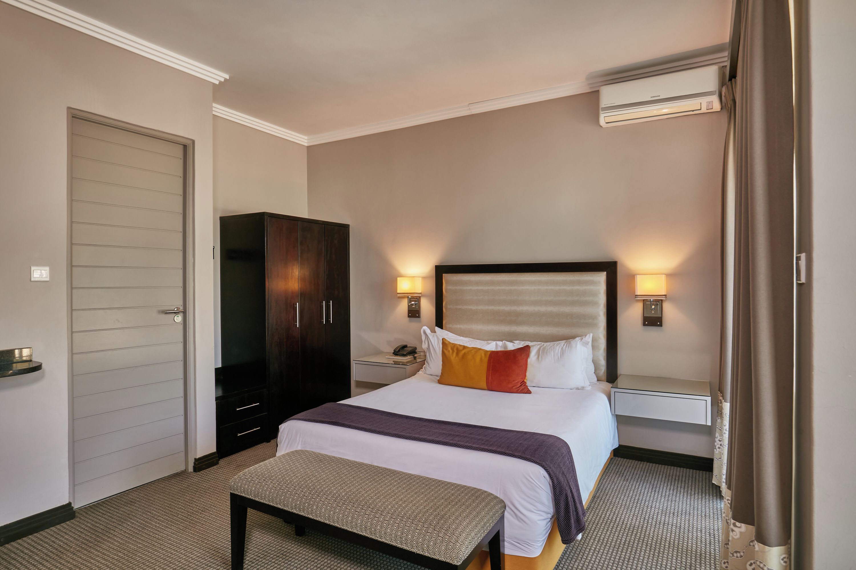 Una habitación de hotel con una cama, mesitas de noche, un armario y un equipo de aire acondicionado.