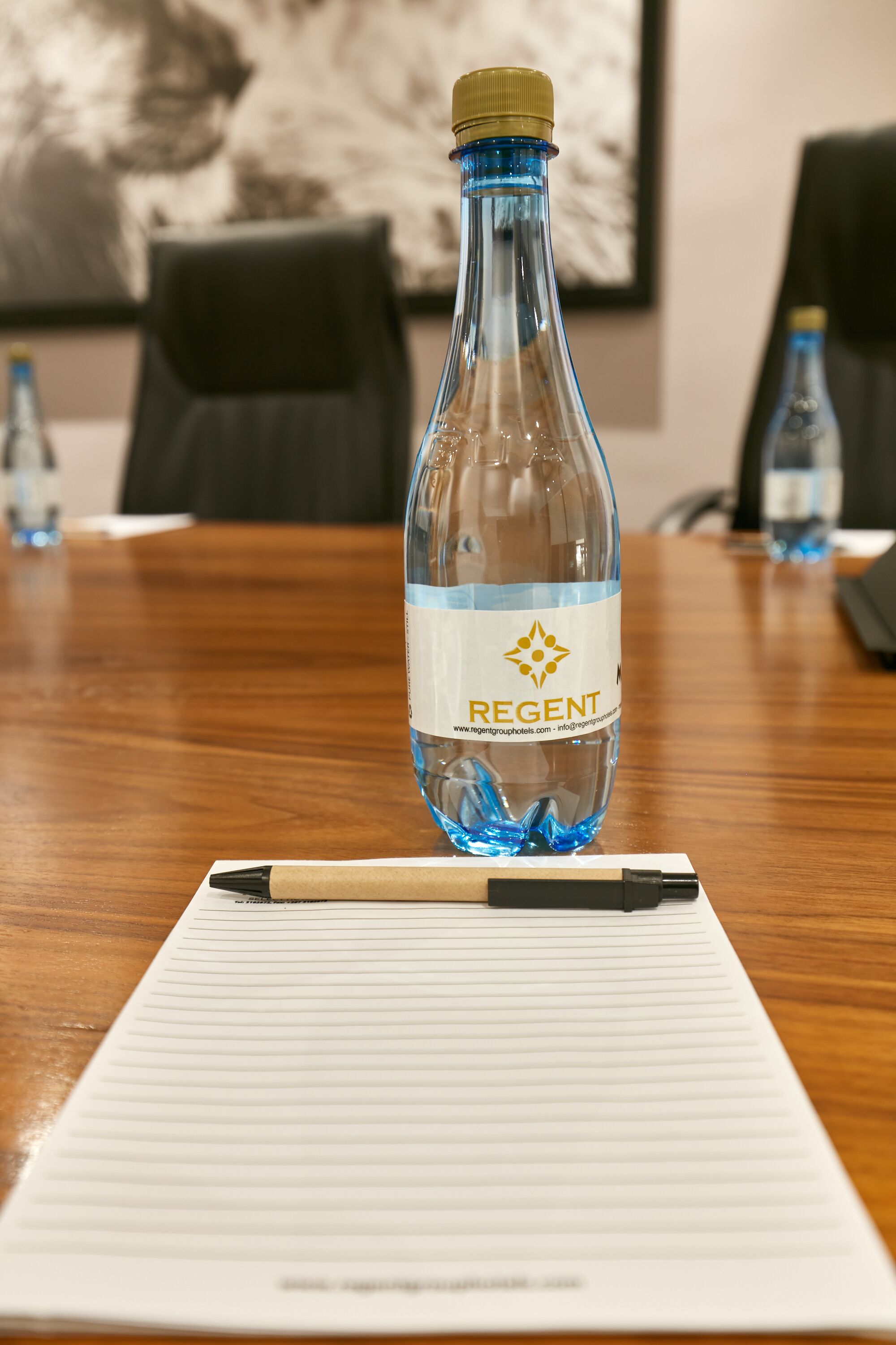 Een fles Regent water op een houten tafel, samen met een notitieboekje en een pen.