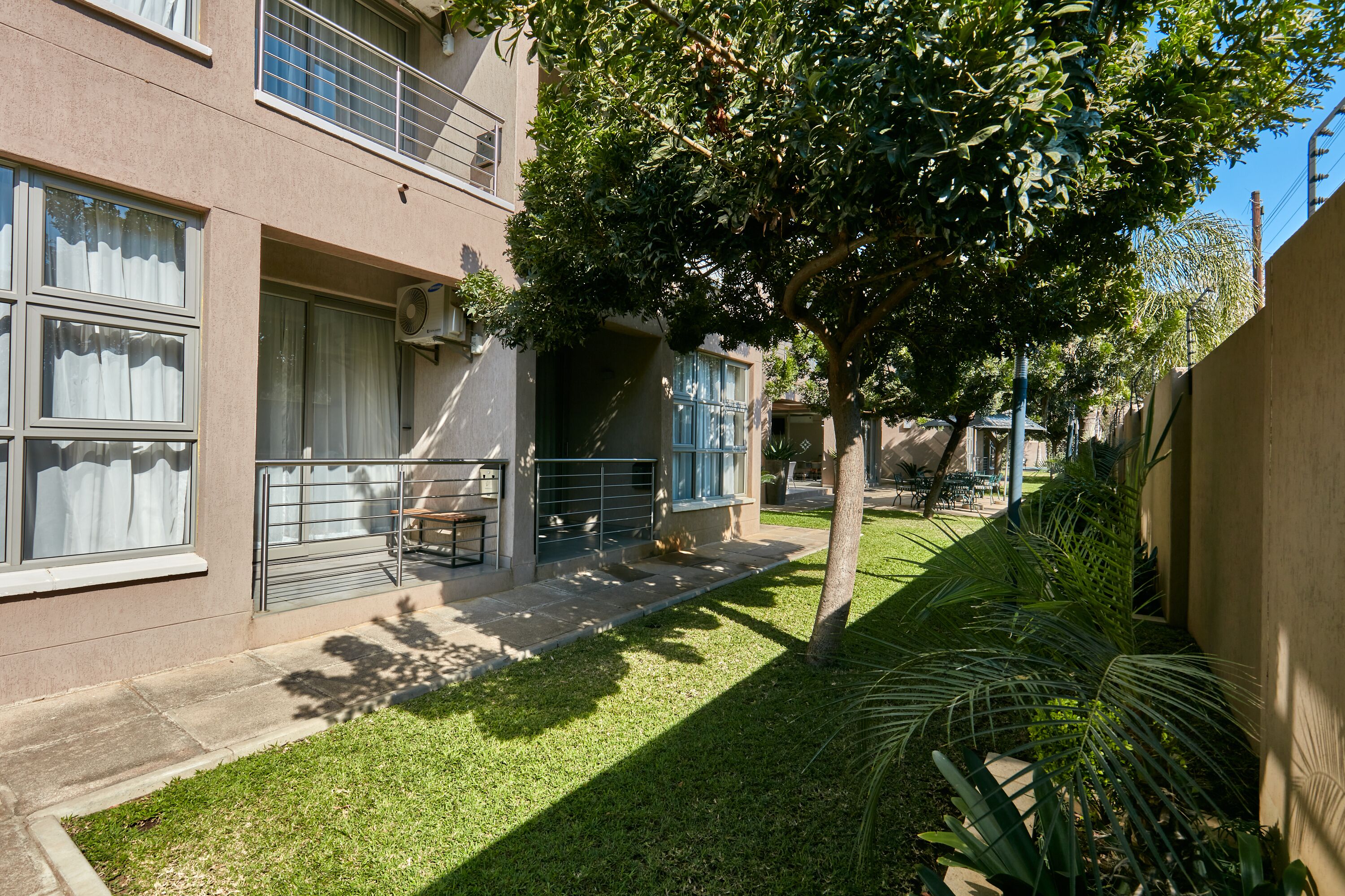 Un edificio residencial con un pequeño jardín delantero, un árbol y un balcón.
