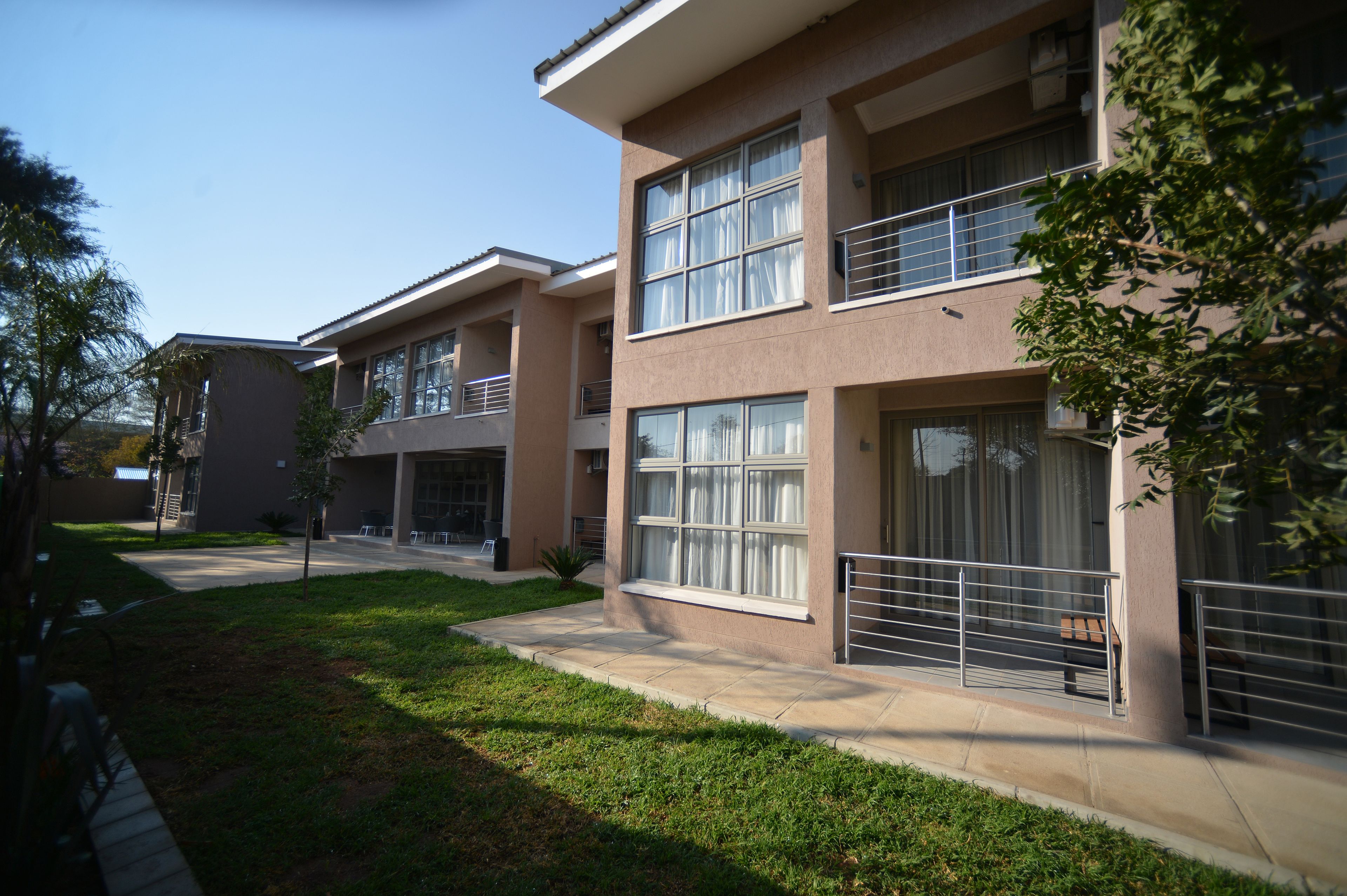 A modern multi-story residential building with large windows, balconies, and a well-maintained lawn.
