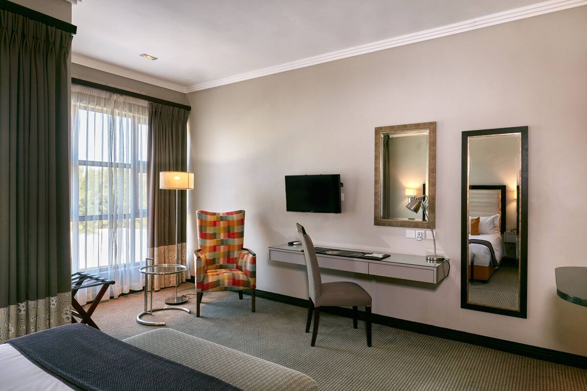 A hotel room with a bed, desk, chair, TV, and two mirrors.