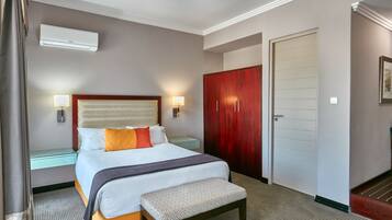 A hotel room with a bed, bedside tables, a wardrobe, and an air conditioning unit.