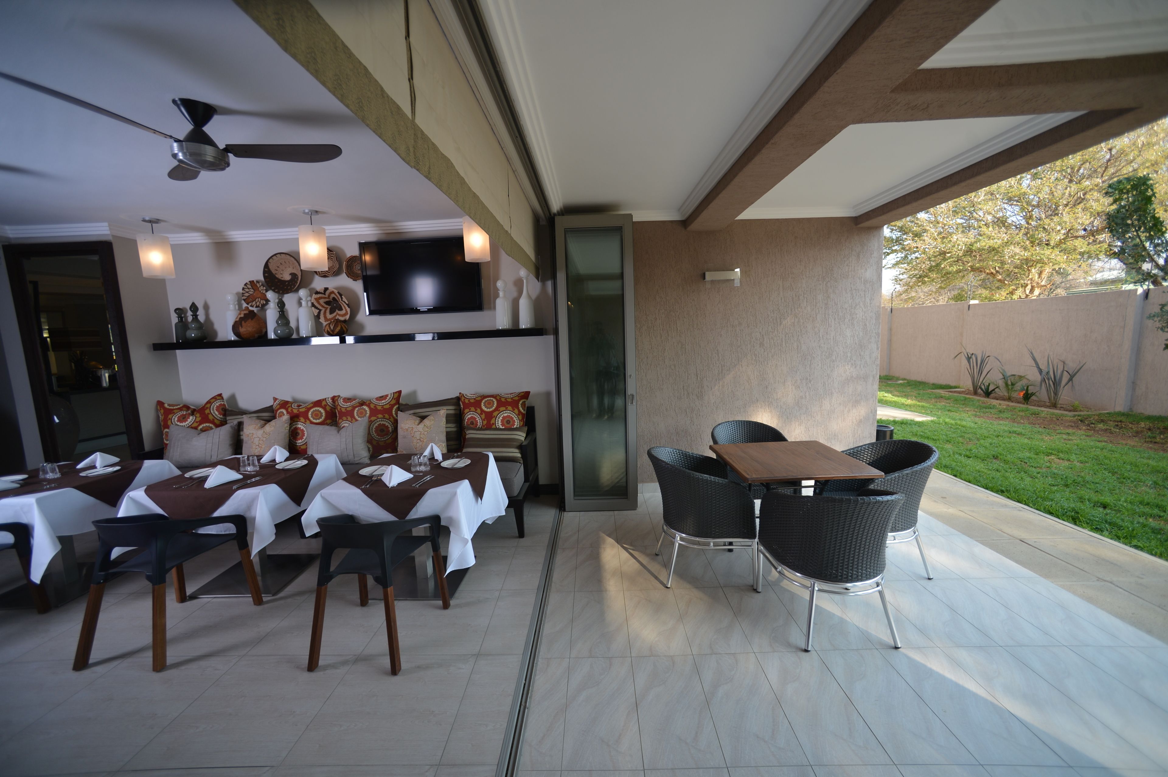 Un espace extérieur aménagé pour les repas, avec des tables et des chaises, un ventilateur de plafond et un téléviseur fixé au mur.