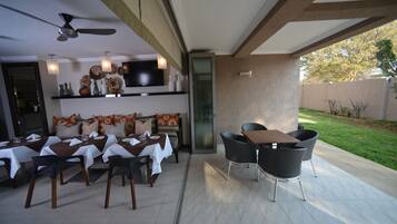 Un espace extérieur aménagé pour les repas, avec des tables et des chaises, un ventilateur de plafond et un téléviseur fixé au mur.