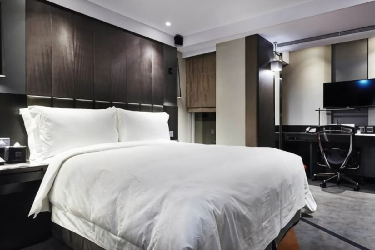 Habitación de hotel con una cama grande, un escritorio, una silla, un televisor de pantalla plana y un armario.