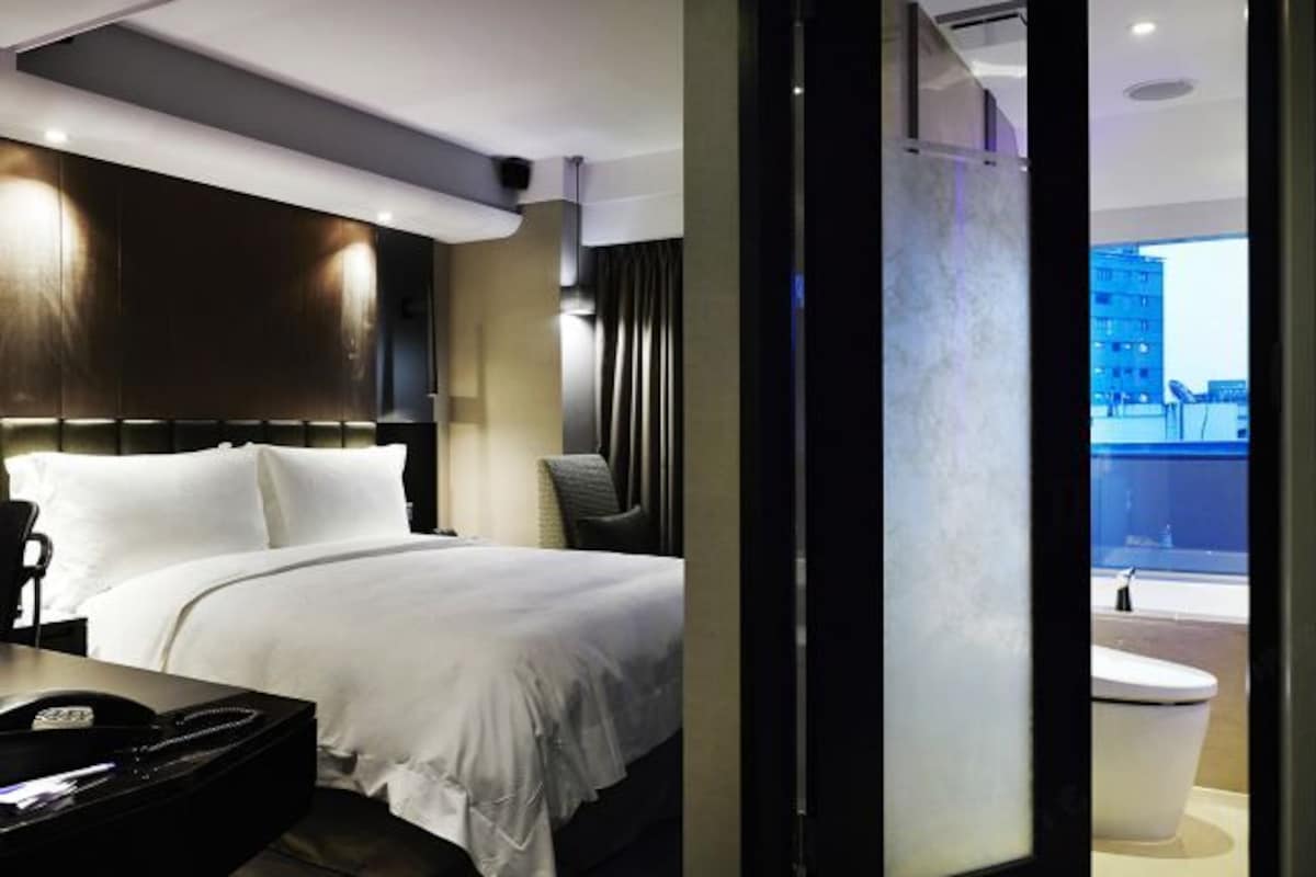 Une chambre d’hôtel moderne, dotée d’un grand lit, d’un bureau et offrant une vue sur le paysage urbain.