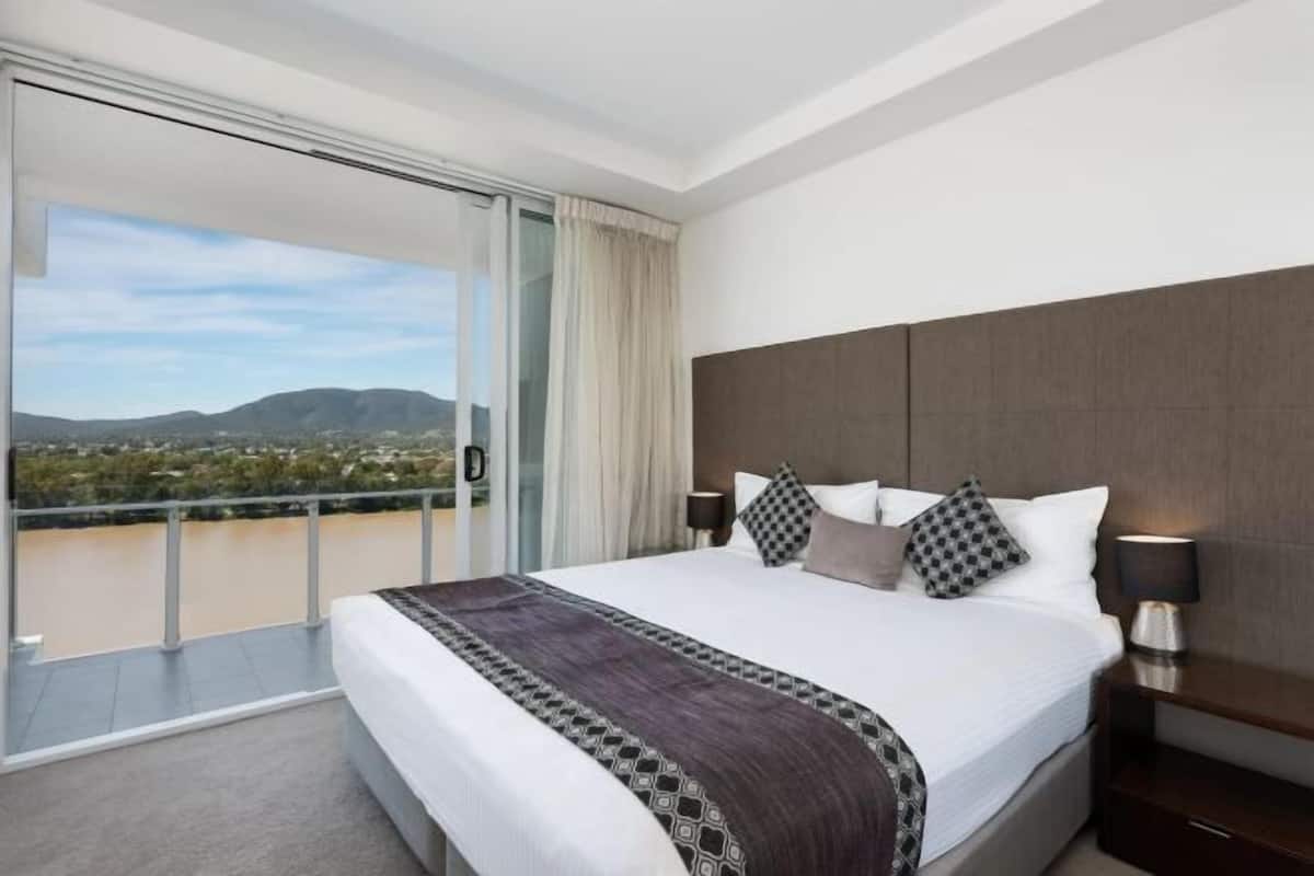 Ein Hotelzimmer mit einem großen Bett, einem Nachttisch, einem Fenster mit Blick auf ein Gewässer und Berge sowie einem Balkon.