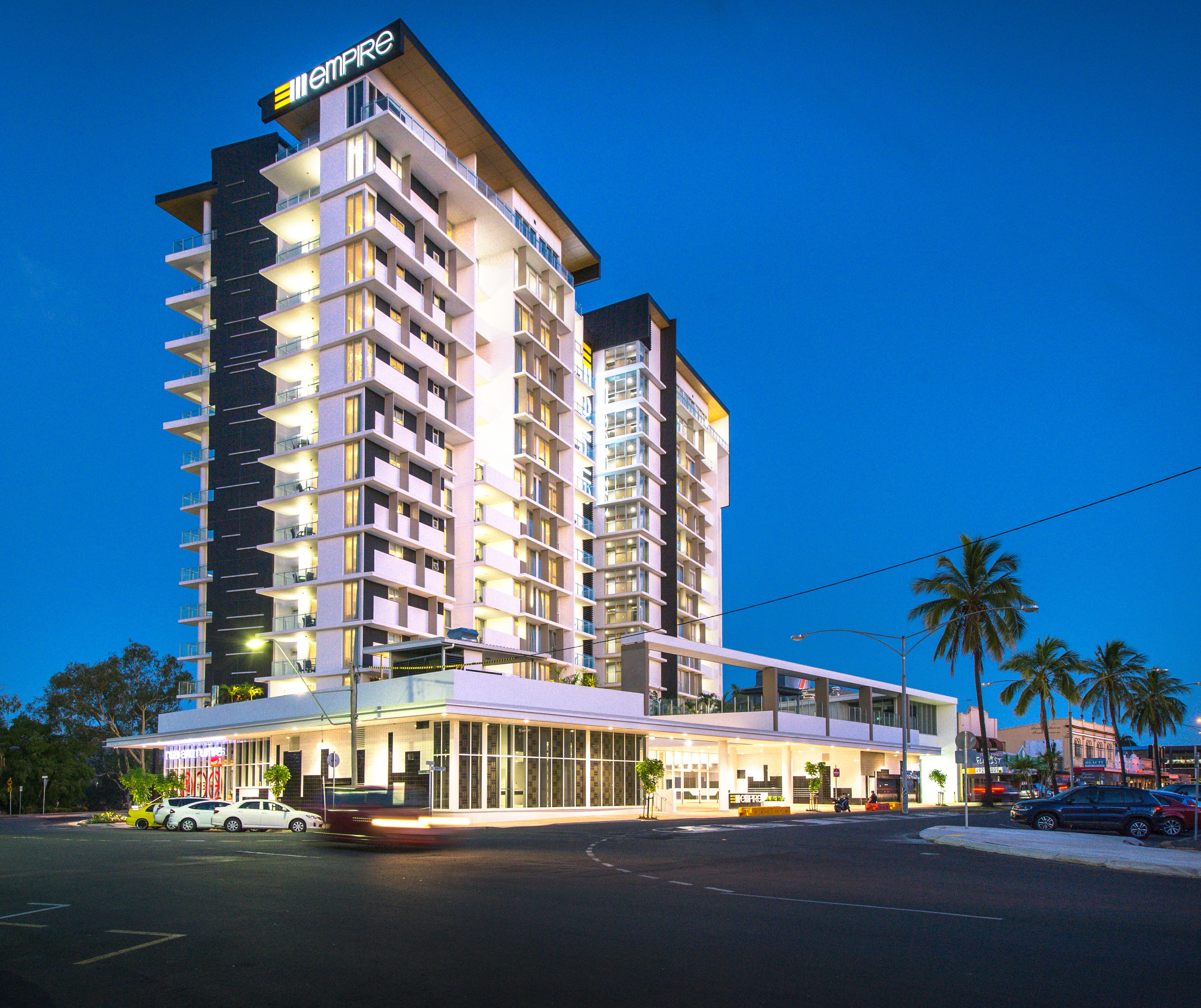A multi-story hotel with a modern design, featuring balconies on each floor, a prominent entrance with glass doors, and a sign indicating the hotel name.