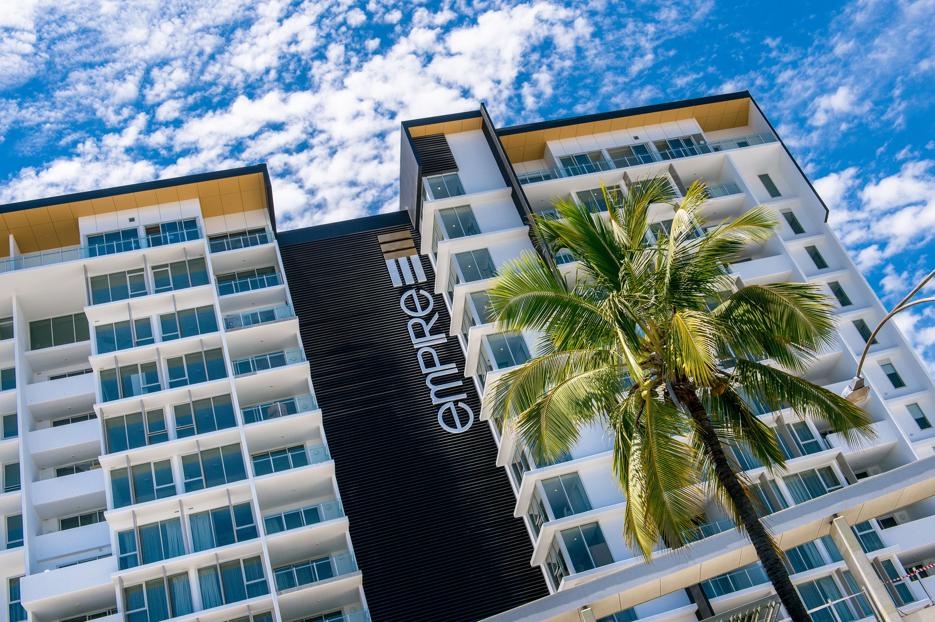 A modern hotel building with a prominent "empire" sign, multiple balconies, and a palm tree in front.
