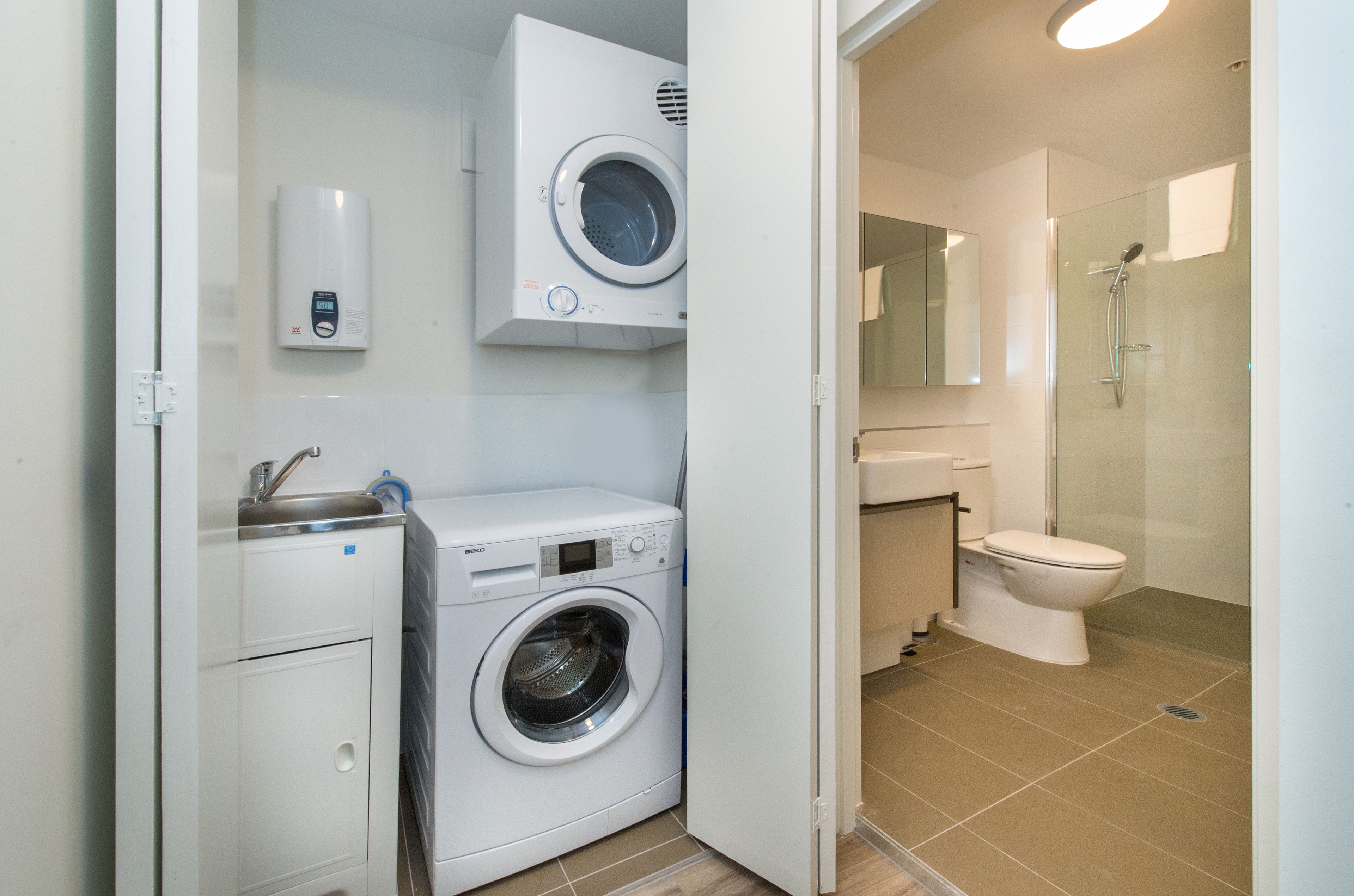 A compact bathroom with a washing machine, a toilet, and a glass-enclosed shower.