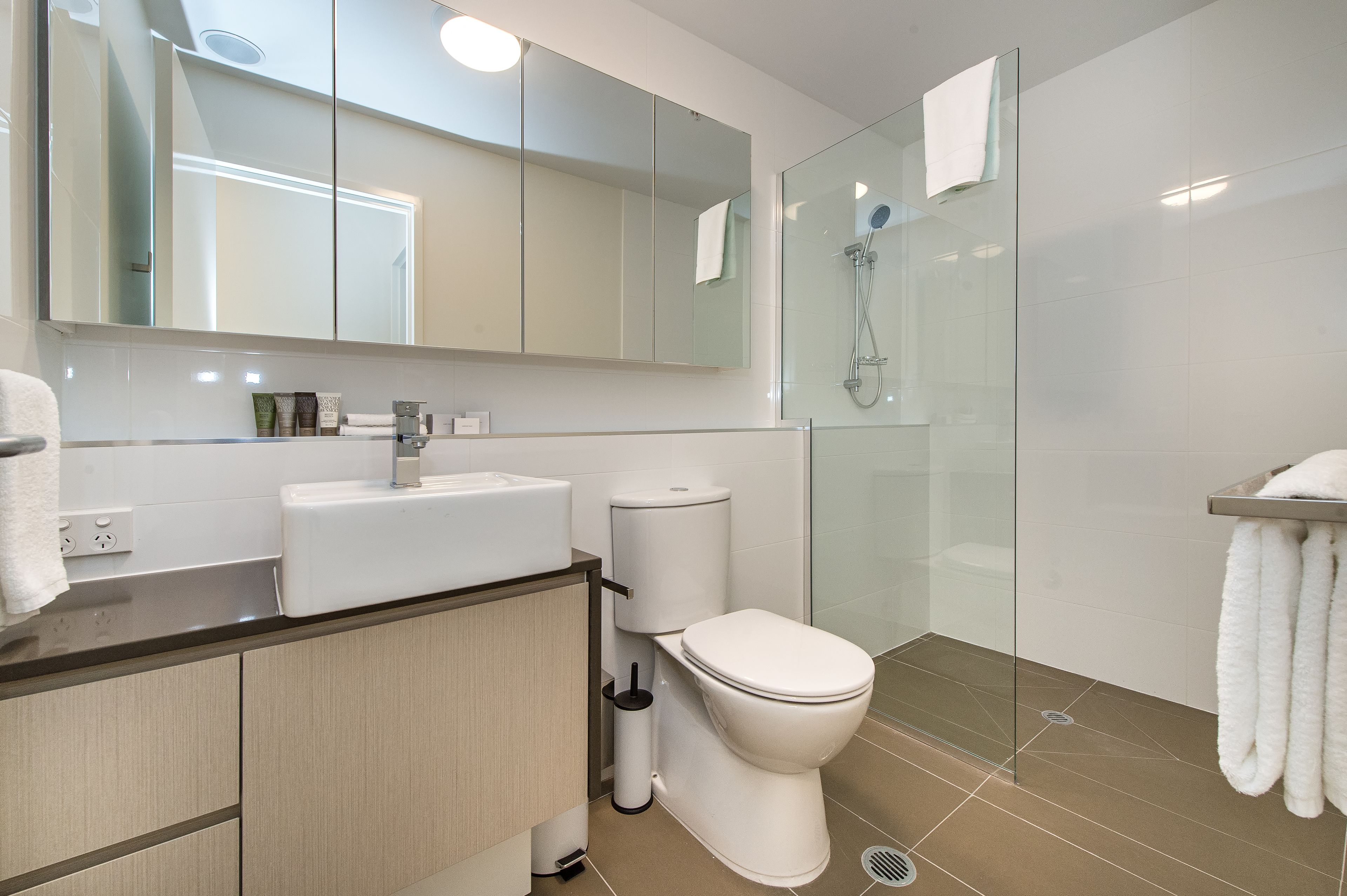 Une salle de bain moderne avec une douche à parois de verre, des toilettes blanches et un meuble-lavabo avec un miroir.