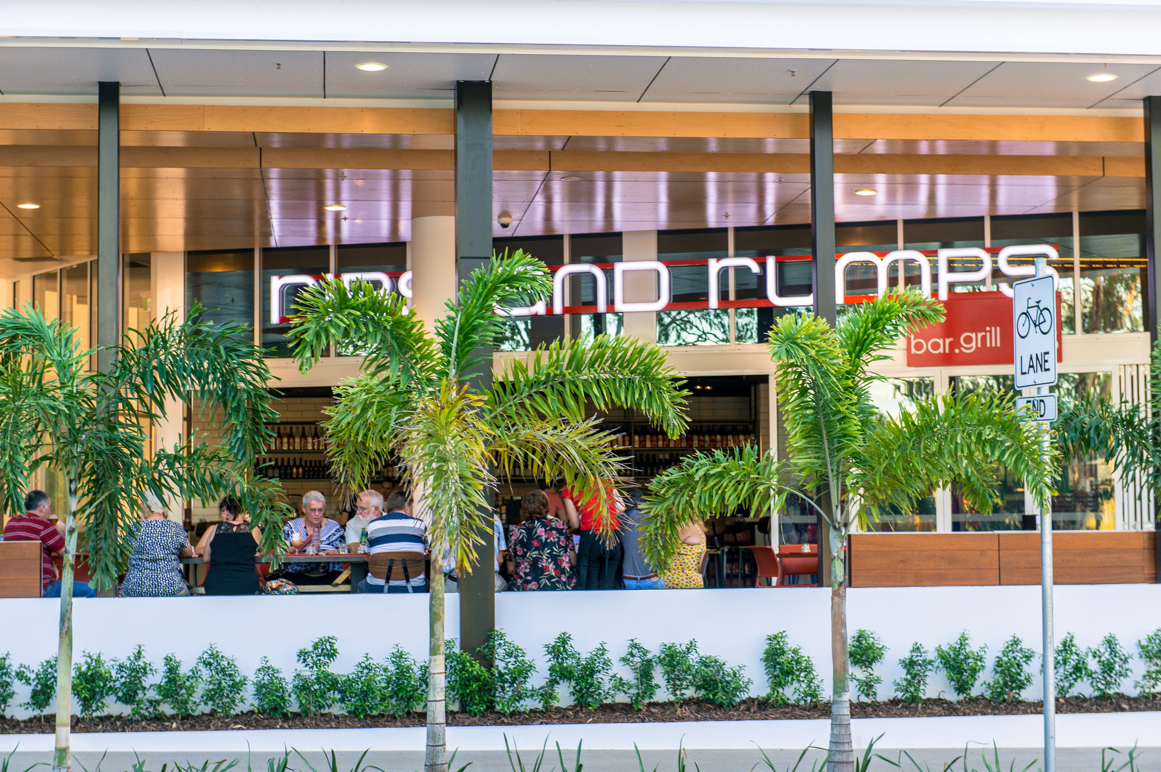 A bar and grill with outdoor seating, palm trees, and a bike lane sign.