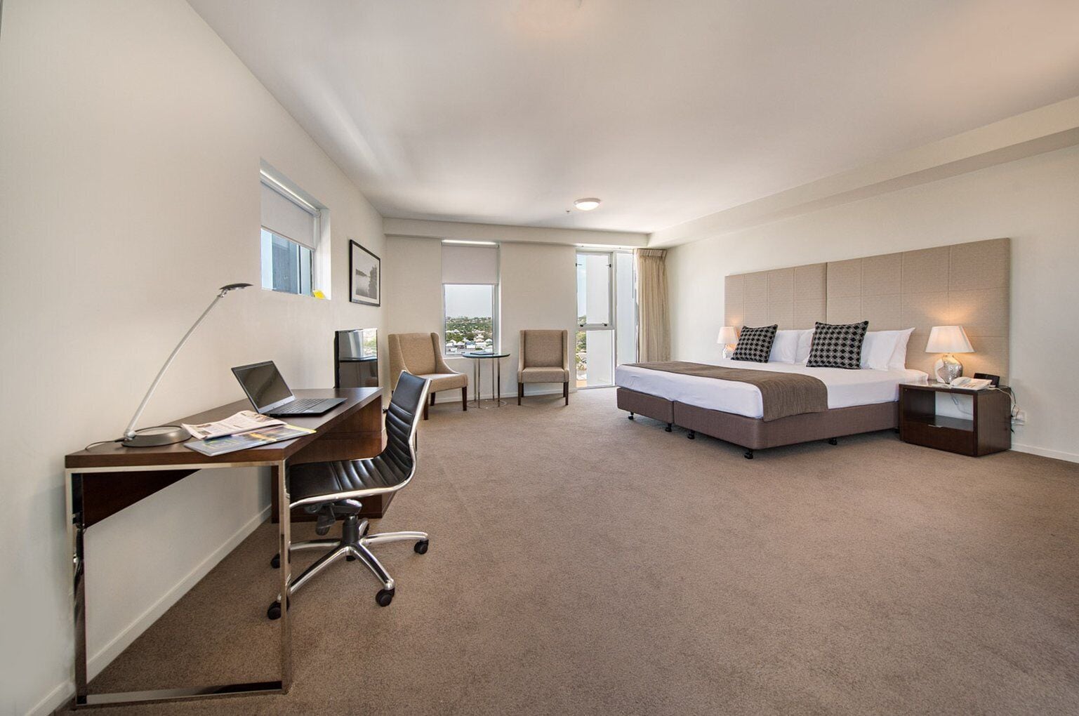 Habitación de hotel con cama, escritorio, silla y vistas al exterior.