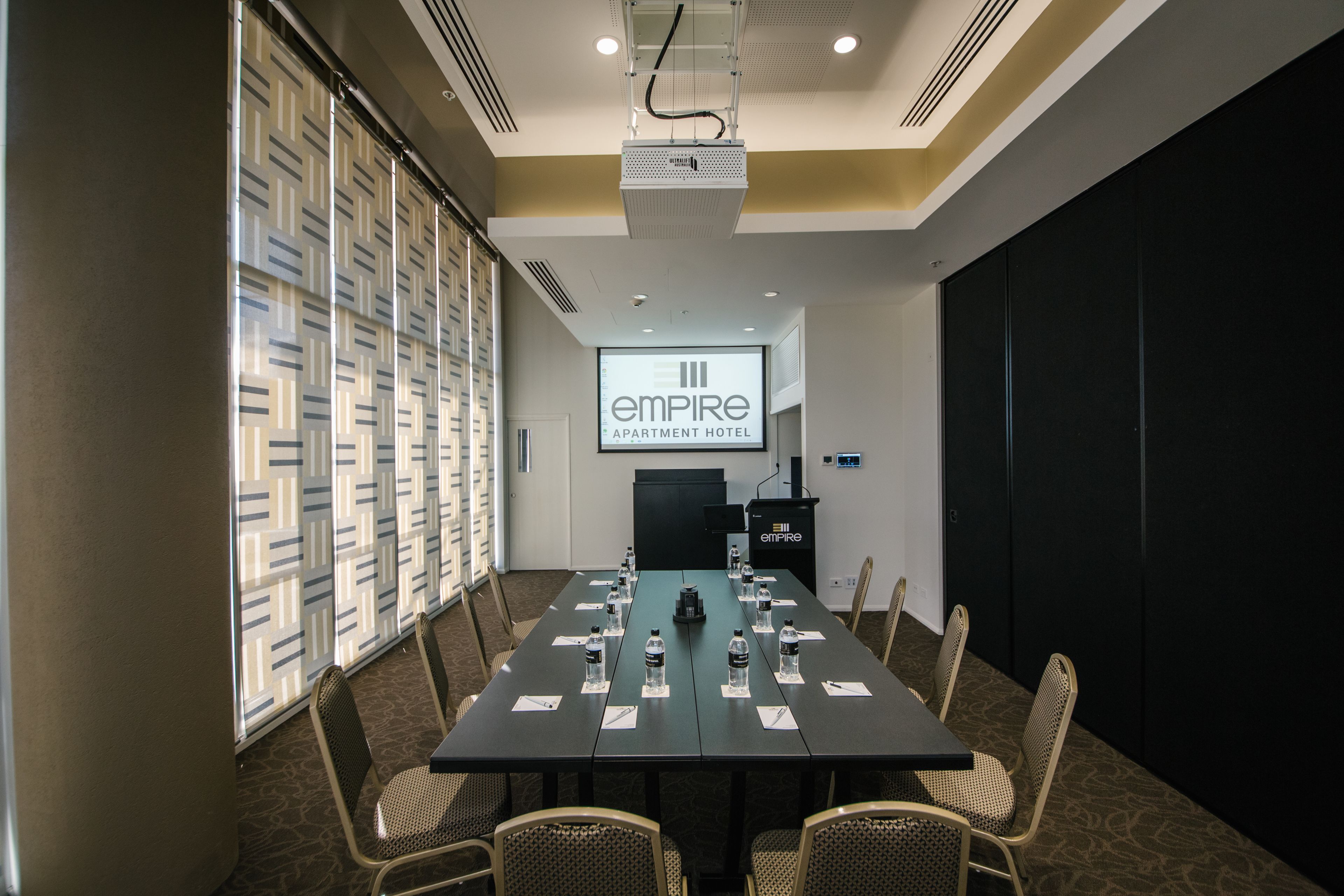 A conference room with a long table, chairs, a projector screen displaying "Empire Apartment Hotel", and a podium.