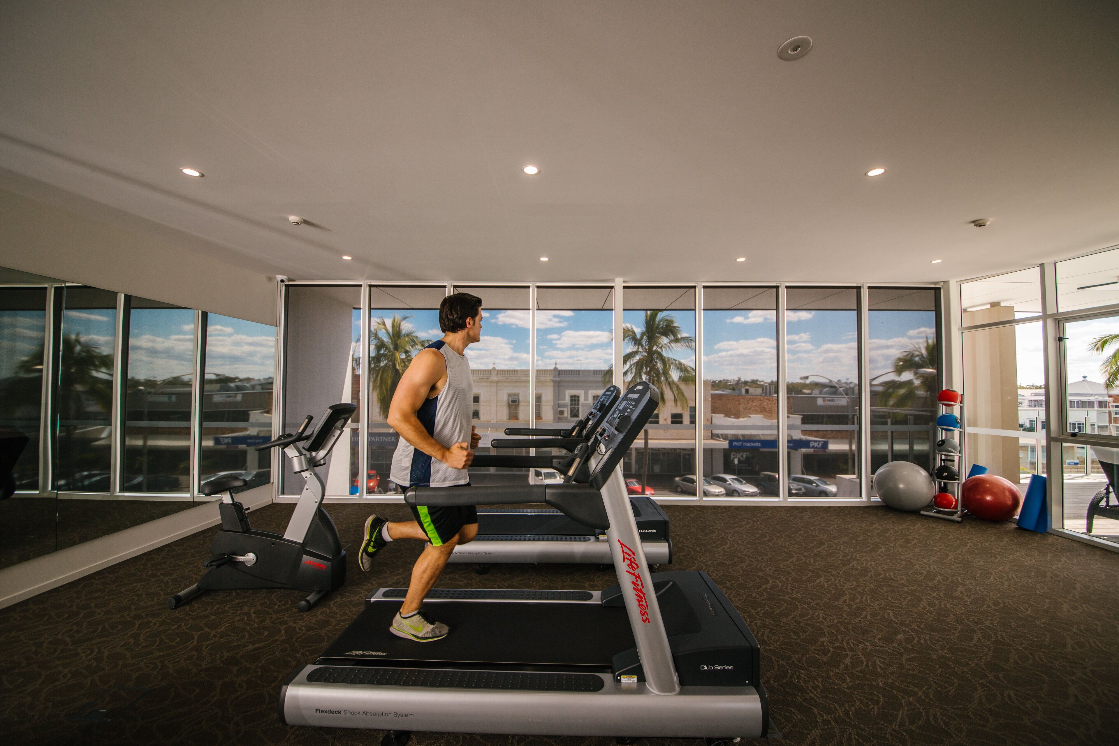 A gym with treadmills, exercise balls, and a large window with a view of palm trees and buildings.