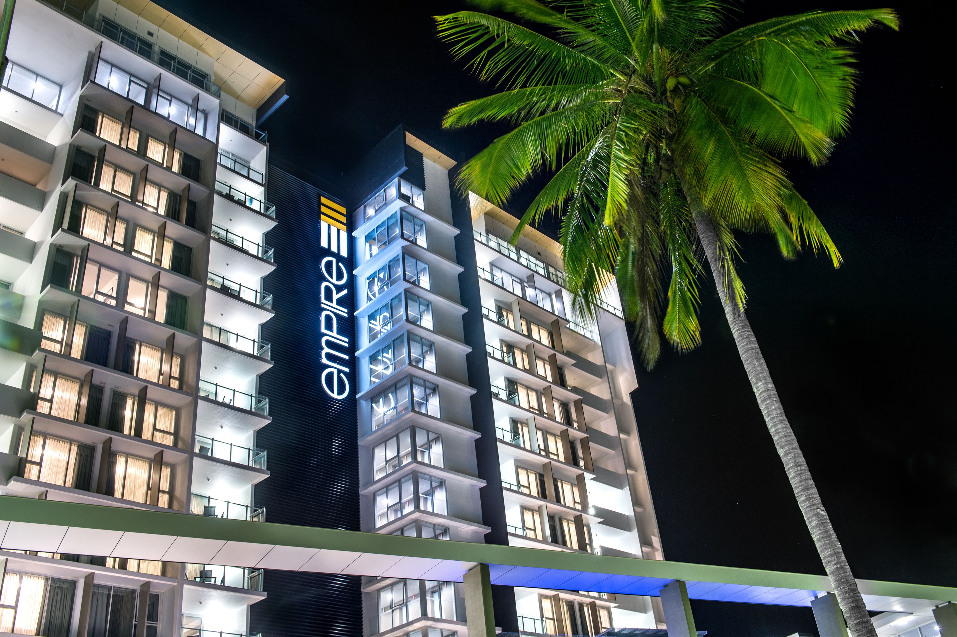 Un hôtel à plusieurs étages, reconnaissable à son grand panneau « enRE », ses balcons et son palmier.