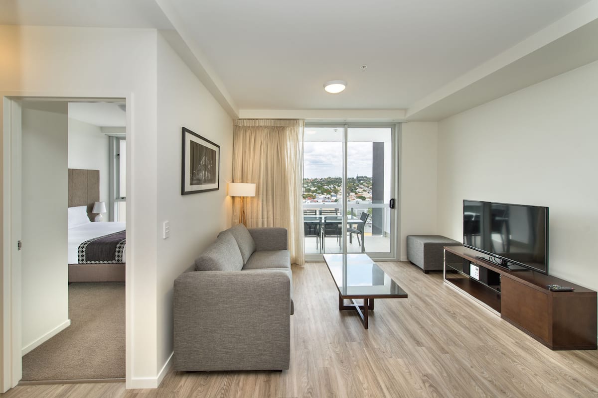 Ein modernes Hotelzimmer mit Sofa, Fernseher, Glastisch und einem Balkon mit Blick.