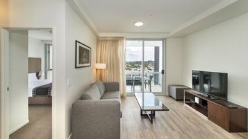 A modern hotel room with a sofa, a TV, a glass table, and a balcony with a view.