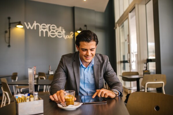 A man in a suit sitting at a table in a modern restaurant with a sign reading "where will you meet?" - Empire Apartment Hotel (Rockhampton)
