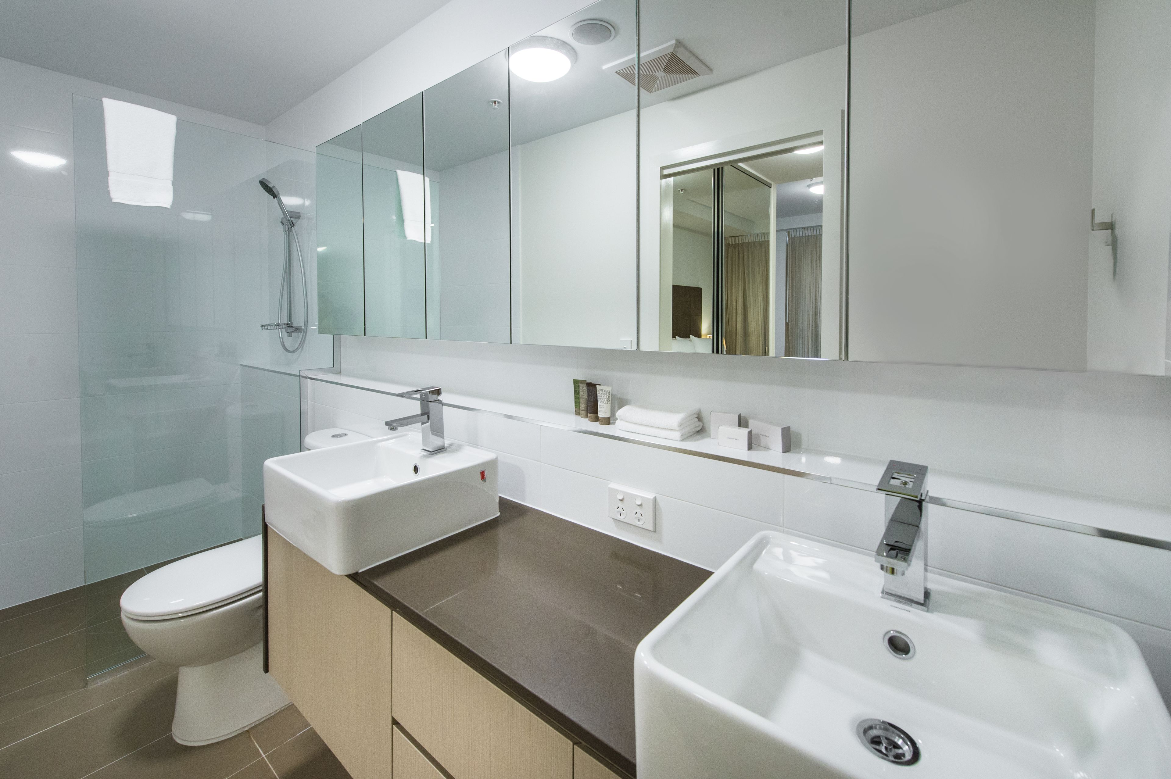 Une salle de bain moderne avec deux lavabos, des toilettes, une douche à l’italienne et un grand miroir.