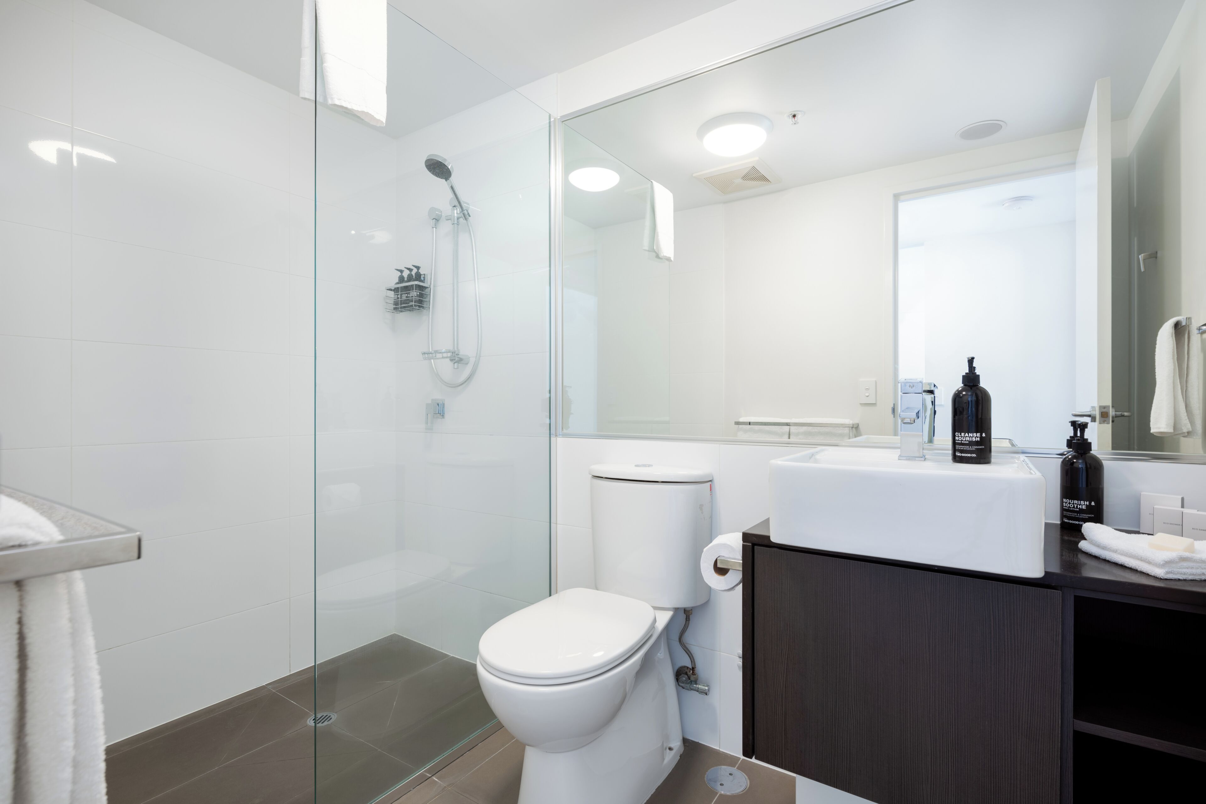 Een moderne badkamer met een douchecabine van glas, een wit toilet, een donker houten wastafelmeubel en een spiegel boven de wasbak.