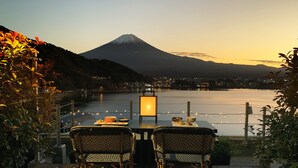 A dining table with two chairs facing a scenic view of a mountain and a body of water. - Mizno Hotel (Fujikawaguchiko)