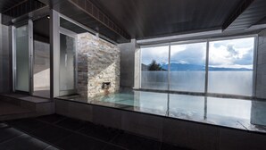 A modern interior with a stone fireplace, large windows, and a view of a mountain range. - Mizno Hotel (Fujikawaguchiko)