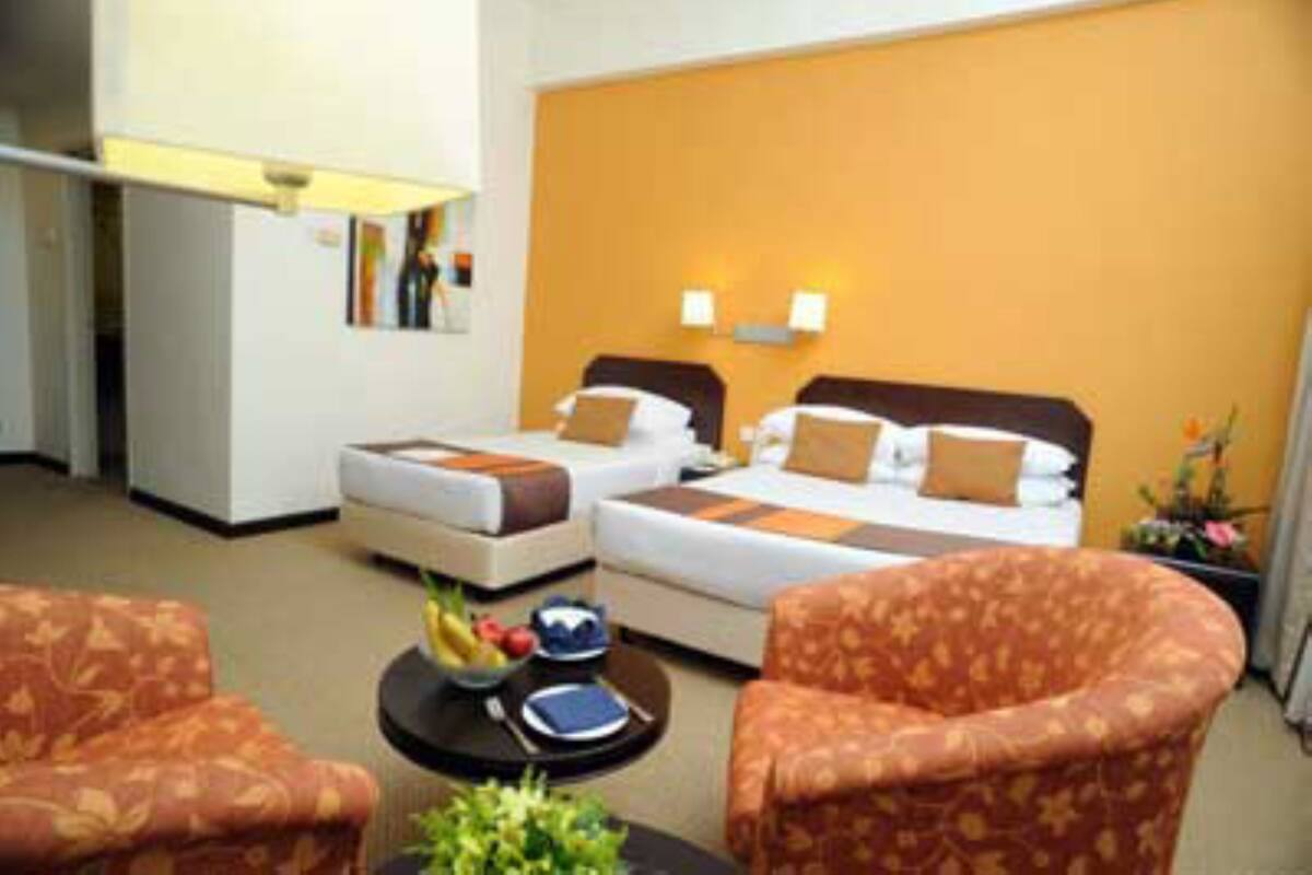 A hotel room with two beds, a small table with a bowl of fruit, and a chair.