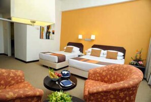 A hotel room with two beds, a small table with a bowl of fruit, and a chair.
