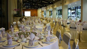 A banquet hall with round tables set for a formal event, featuring white tablecloths, neatly folded napkins, and silverware. - RHR Hotel at Uniten (Kajang)