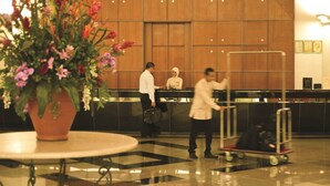 A lobby with a reception desk, a large potted plant, and a luggage cart. - RHR Hotel at Uniten (Kajang)