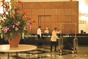 A lobby with a reception desk, a large potted plant, and a luggage cart.