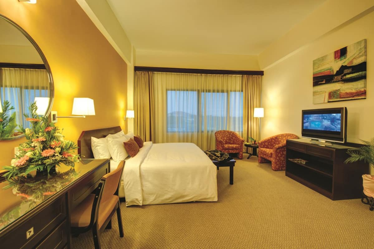 A hotel room with a bed, a desk, a chair, a television, and a painting on the wall.