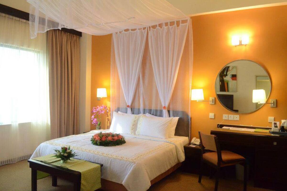 A hotel room with a bed, bedside table, chair, desk, and a mirror.