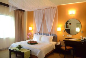 A hotel room with a bed, bedside table, chair, desk, and a mirror.