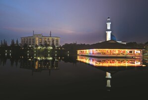 A waterfront hotel with a reflection in the water, a prominent building with a tower, and a boat docked nearby.