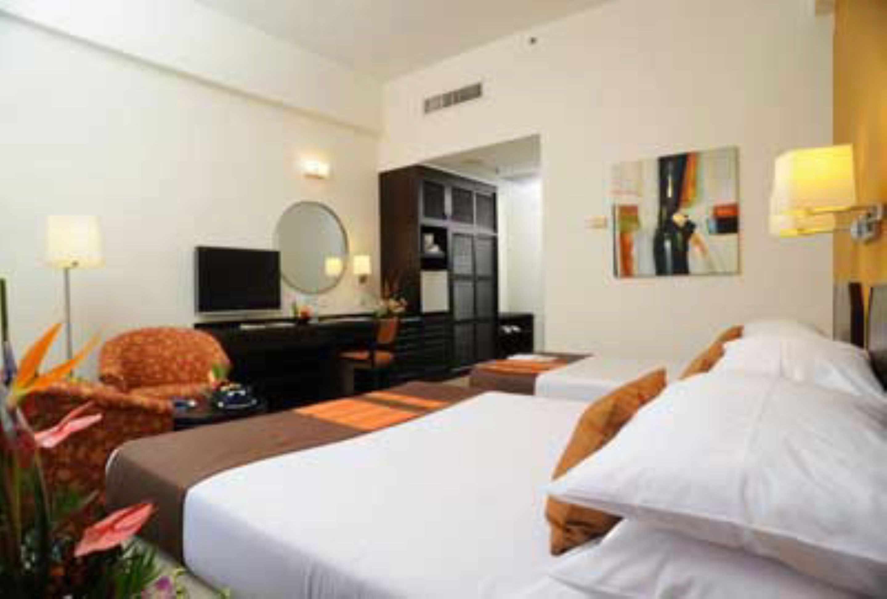 A hotel room with a large bed, a desk with a chair, a television, and a wardrobe.