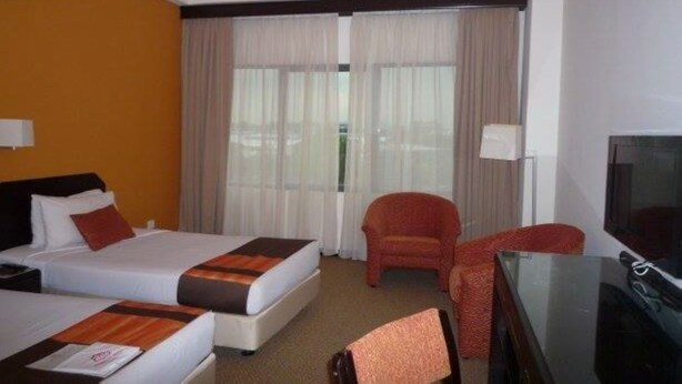 A hotel room with two beds, a television, a chair, and a window with curtains.